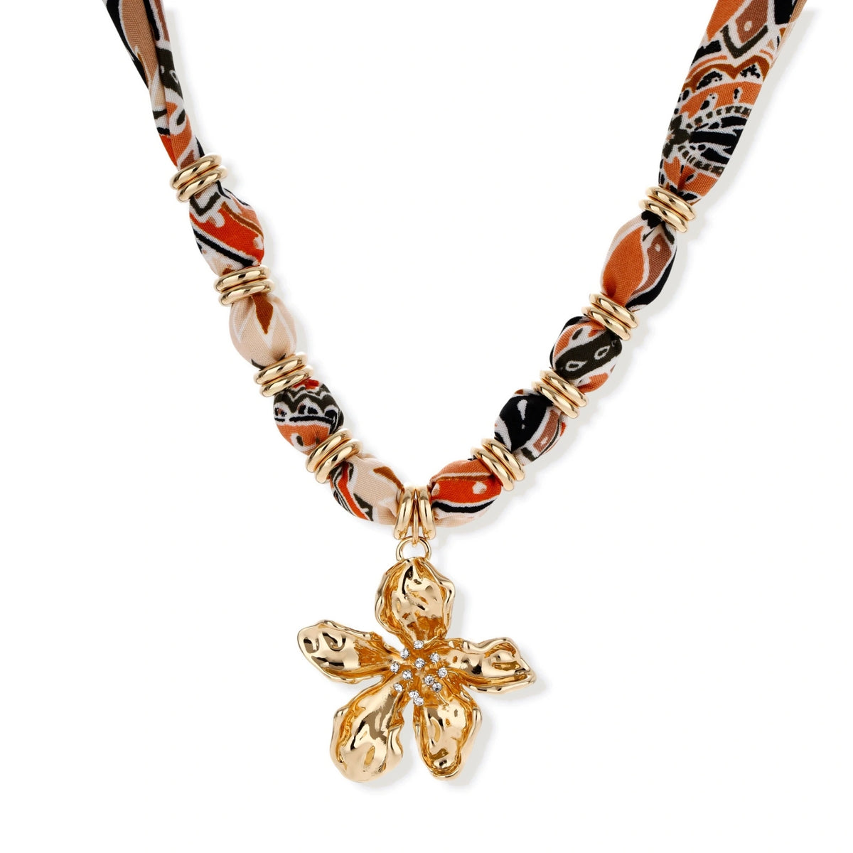 Vibrant patterned fabric necklace with gold-toned flower pendant featuring rhinestone center on white background